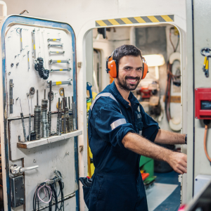 Photo of a man with ear defenders on at the entrance to the engine room on a cargo ship.