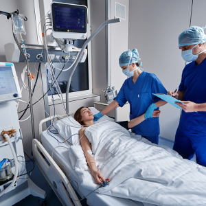 Photo of a female patient in a hospital intensive care bed with two nurses in PPE standing next to the bed.