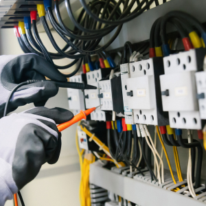 Image of hands wearing protective gloves testing an electrical control panel
