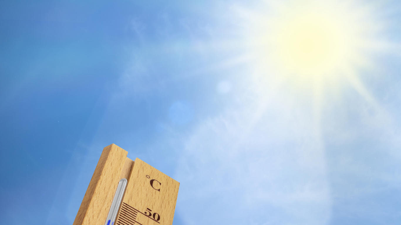 A blue sky with bright sunshine showing the top of a wooden thermometer.